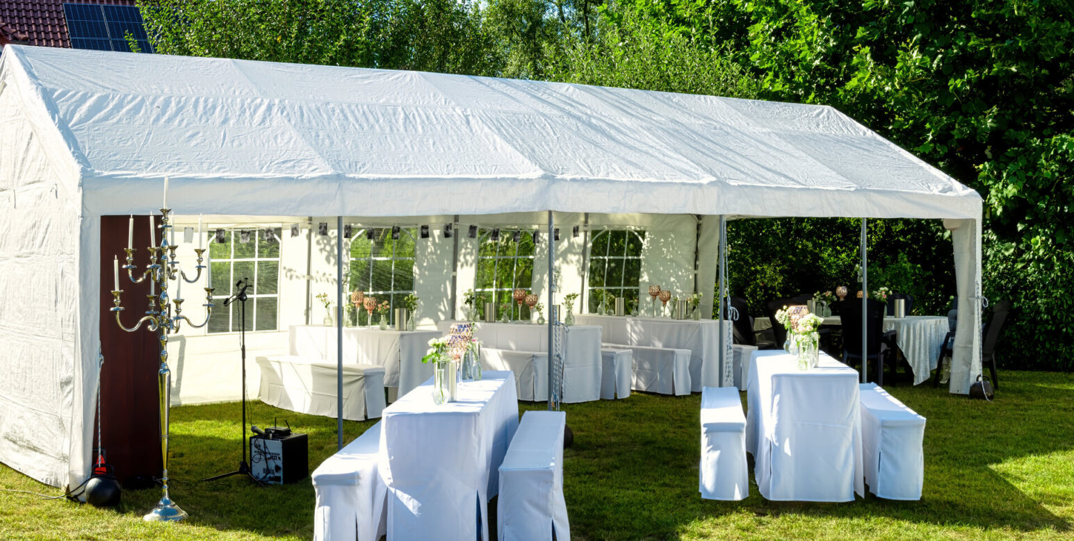 Weißes Zelt mit Hochzeitstischdekoration, dekoriert mit frischen Blumen, Champagnerkühlern und dekorativen Gläsern für eine Feier