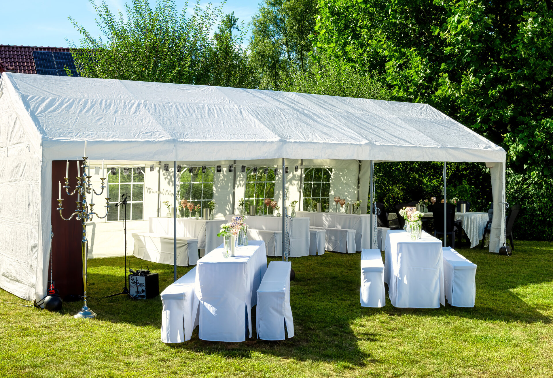 Weißes Zelt mit Hochzeitstischdekoration, dekoriert mit frischen Blumen, Champagnerkühlern und dekorativen Gläsern für eine Feier